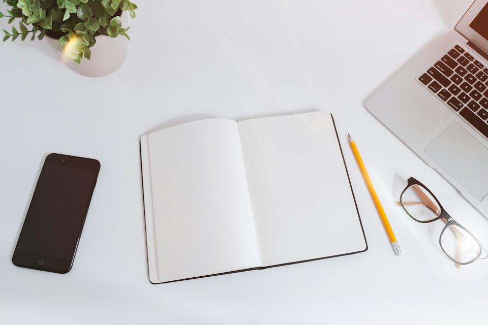 An open notebook and pencil beside a laptop on a work table
